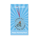 Blue backer card with rays radiating from the center and white text reading ‘Scott Aukerman’s Comedy Bang! Bang!’ at the top. The ornament attached shows a person on a motorcycle with the words ‘COMEDY BANG! BANG!’ around the design, hanging from a red ribbon. Text at the bottom reads ‘Happy Heynong Days!’