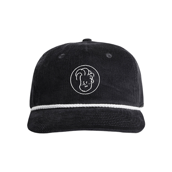 A black corduroy cap with a white embroidered circular logo on the front, featuring a simple line drawing of a face with swooped hair. The hat has a white decorative rope along the brim.