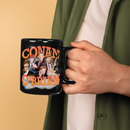 A person wearing a green jacket holds a black mug featuring the orange ‘CONAN O’BRIEN’ collage design, showing Conan O’Brien in various expressions and outfits.
