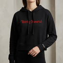 Lifestyle view of a black cropped hoodie worn by a model. The front features large red gothic blackletter text reading ‘Weirdly Immortal’ across the chest. The hoodie has a drawstring hood, cropped fit, long sleeves, and a small print near the wearer’s left cuff reading ‘MORBID Live’.