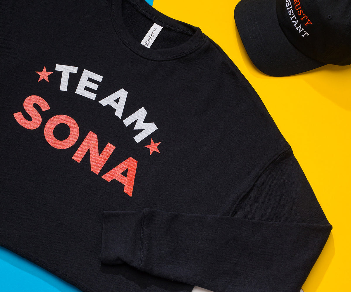 Team Sona Tshirt on a yellow desk with a hat in the corner.