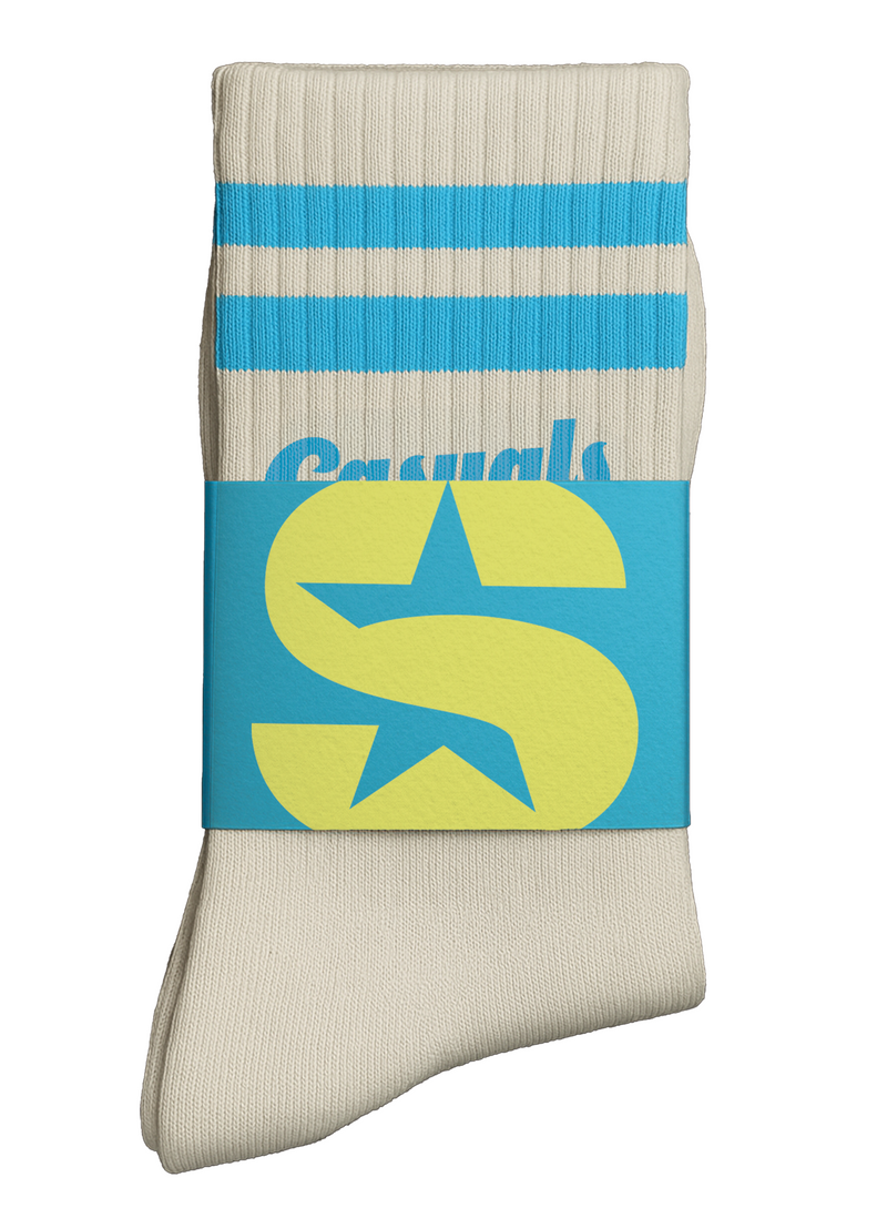Pair of cream ribbed crew socks with two sky-blue stripes at the cuff, folded with a branded wrap showing the SiriusXM 'S-Star' logo in yellow and blue. The word ‘Casuals’ in blue script is partially visible beneath the band.