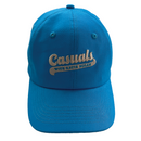 Straight-on view of a bright blue baseball cap featuring beige embroidery of the ‘Casuals with Katie Nolan’ logo centered on the front panel.