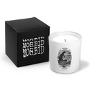 Front product image of a white candle in a glass jar beside a black box printed with ‘MORBID MORBID MORBID’ in distressed white lettering. The candle features a detailed black illustration of a skeleton in a hooded cloak rowing a small boat, framed by ornate scrollwork, with small text reading ‘MORBID 2018’ and ‘SHE BECOMETH SO LAME’.