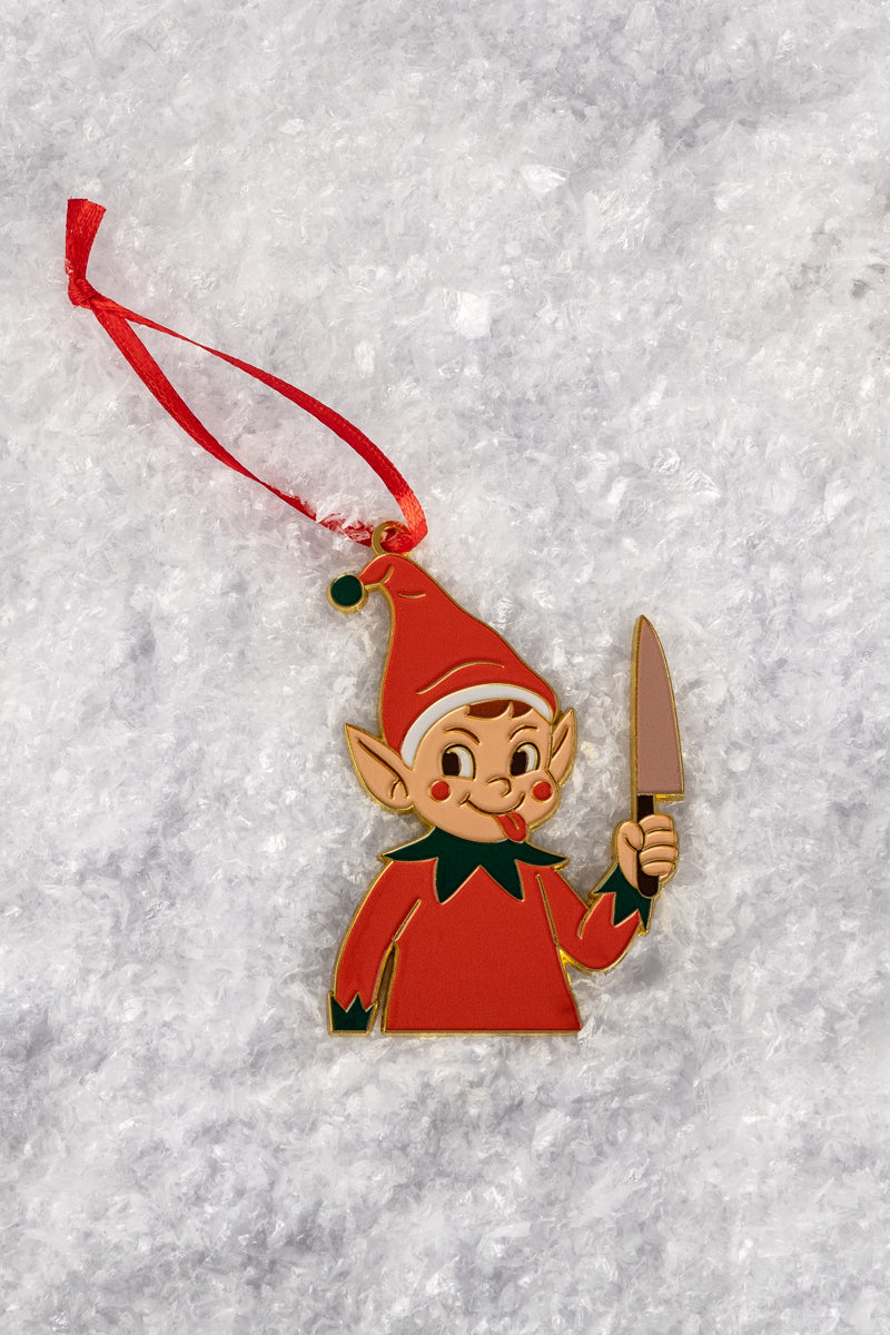 A close-up of the elf ornament featuring a smirking elf in a red outfit and hat with a green collar, holding a knife aloft against a snowy backdrop.