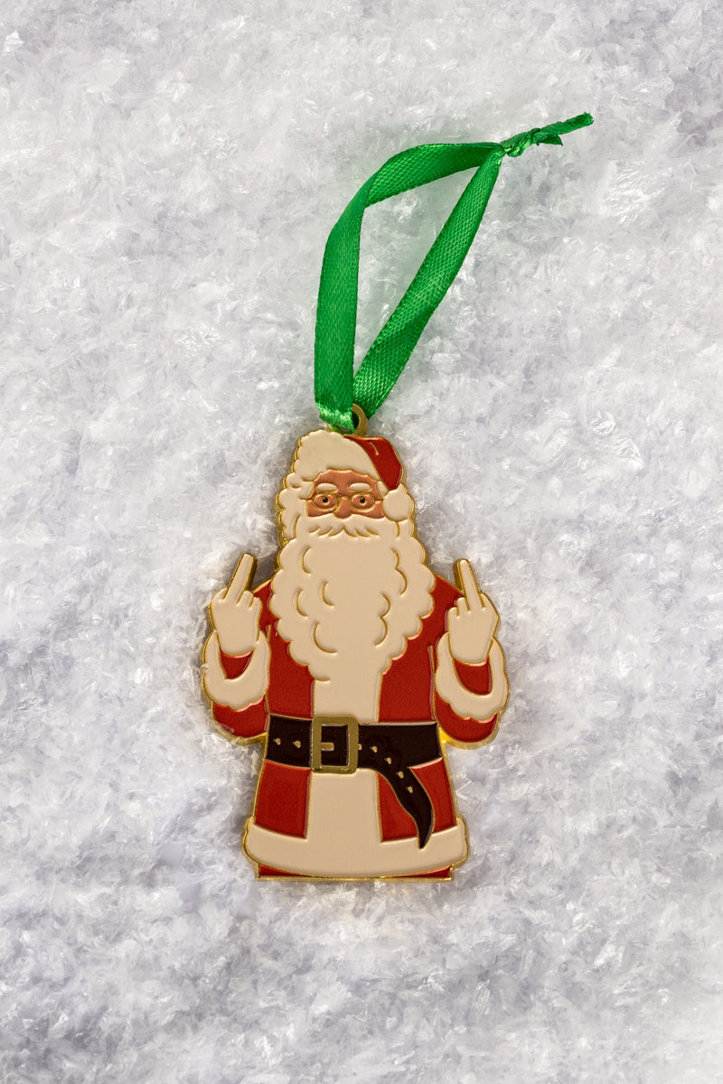 A close-up of the Santa ornament featuring Santa Claus in red and white attire, holding up both middle fingers, hanging from a green ribbon against a snowy background.