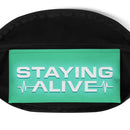 Close-up view of the interior pocket of a fanny pack, showing a mint green fabric lining printed with bold white text that reads 'STAYING ALIVE' in all capital letters. Stylized EKG heartbeat line graphics appear before and after the word 'ALIVE'.
