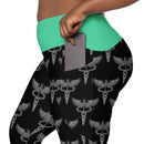 A close-up of someone placing a phone into the pocket of black leggings, which feature a green waistband and a grey caduceus print (a winged staff with two snakes).