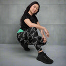 A person squatting while wearing black leggings with an all-over pattern of white caduceus symbols, a winged staff with two snakes, representing medicine. The leggings have a contrasting green waistband.