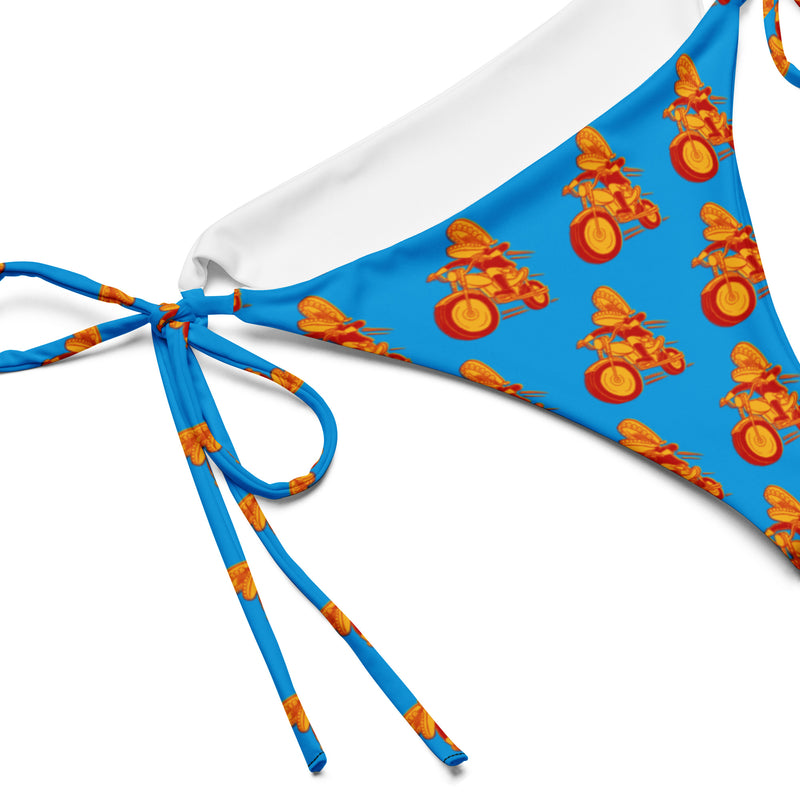 A close-up view of the right side of a blue bikini bottom showing the side tie and repeating motorcycle character graphic, with visible white lining inside the edge seam.
