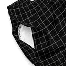 A close-up of the outer side of the black swim trunks, showing the white grid pattern and a partial view of the white mesh pocket lining inside. The waistband is gathered with elastic, and no visible logos or text are present.