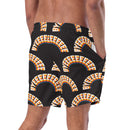A man wearing black swim trunks printed with a repeating pattern of arched rainbow 'BYEEEEEEE' graphics, shown from the back with his right hand in the pocket.