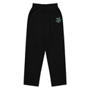 A flat lay of black unisex wide-leg joggers with an elastic waistband, drawstring, and a 'STAYING ALIVE' graphic on the left leg, incorporating a caduceus symbol (a winged staff with two snakes) in gray and green.