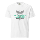 White heavyweight T-shirt featuring a large graphic of a caduceus (a winged staff with two snakes) centered on the chest, with the words 'STAYING ALIVE' in bold mint green lettering and 'Jon Gabrus' and 'Adam Pally' in black text below, flanked by ECG line motifs.