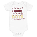 White baby onesie with text 'I'm not a FOODIE I'm an EATER' and illustrations of food items.