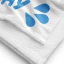 Close-up of white towel fabric showing soft, looped terry texture and stitched edge. Part of the blue splash graphic is visible, highlighting print quality and material thickness.