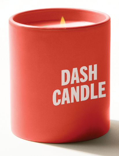A red candle jar with a lit flame and white text on the front that reads ‘DASH CANDLE.’
