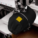 A black cap with a yellow square on a sewing machine.