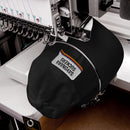 Black dad hat shown under an embroidery machine, mid-production. The upside-down white speech bubble patch is being stitched with the phrase 'SAYONARA SUCKERS' and colorful stripe accents.