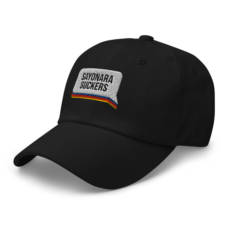 Side view of a black dad hat showing the white embroidered 'SAYONARA SUCKERS' patch with red, orange, blue, and yellow stripes along the base of the speech bubble.