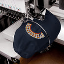 A navy blue dad hat in the process of being embroidered by a machine, stitching the curved 'BYEEEEEEEE' design in multicolored thread across the front.