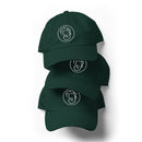 Three dark green spruce dad hats stacked vertically against a light background. Each hat features the same white embroidered circular logo with Conan O’Brien’s stylized face and distinctive hair on the front. The curved brims overlap slightly, showing the layered arrangement.