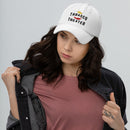 A woman wearing a white dad hat embroidered with the phrase 'The TABASCO THEATER' and a red chili pepper icon, styled with a dusty rose T-shirt and black denim jacket.