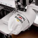 A close-up of a white dad hat being embroidered on a machine, stitching the text 'The TABASCO THEATER' with a red pepper graphic and yellow 'The'.