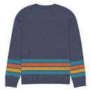 Back view of a navy blue sweater featuring colorful horizontal stripes in blue, orange, yellow, and blue (repeated) across the lower part of the garment and sleeves.