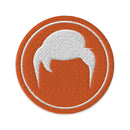 Embroidered patch featuring stylized white hair on an orange circular background