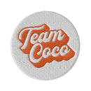 Embroidery patch featuring the words 'Team Coco' in orange and white on a textured background.