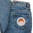 denim jeans with a round embroidered patch featuring a stylized hair design on the back pocket
