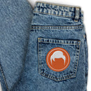 Denim jeans pocket with orange circular patch featuring a white design resembling hair.