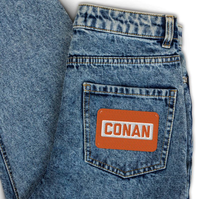 Denim jeans with orange label on back pocket featuring the word 'CONAN'.