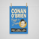 Vertical blue poster hanging from a thin string with two small wooden clothespins at the top corners. The design reads ‘TEAM COCO PRESENTS’ above large cream-colored block letters spelling ‘CONAN O’BRIEN’. Below, in script, it says ‘Needs a Friend’. Conan O’Brien’s illustrated head appears inside a yellow sunburst shape near the lower right. A black banner at the bottom reads ‘FEATURING THE VOICES OF CONAN O’BRIEN × SONA MOVSESIAN × MATT GOURLEY AND YOUR FAVORITE CELEBRITY GUESTS!’.