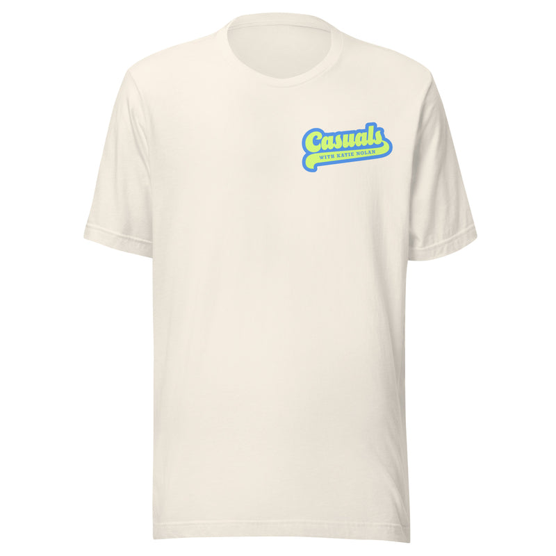 Front view of a vintage white unisex T-shirt featuring the phrase 'Casuals' in blue script with a bold yellow drop shadow, and 'WITH KATIE NOLAN' printed in small yellow uppercase text beneath.