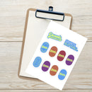 Angled top view of the 'Casuals with Katie Nolan' sticker sheet placed on a clipboard over a light wooden surface. The white rectangular sheet features two text stickers at the top—'Casuals WITH KATIE NOLAN' and 'SPORTS. BUT CHILL.'—and eight oval logo stickers in blue, red, purple, and brown tones.