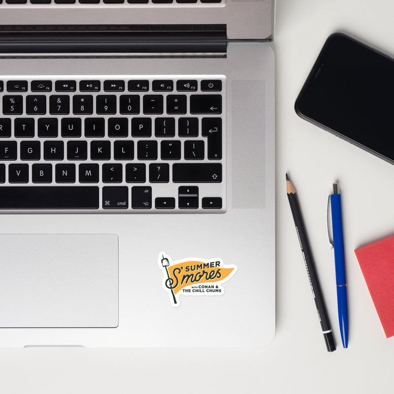 Laptop keyboard with a colorful sticker that reads Summer S'mores with Conan & The Chill Chums, alongside stationery items.