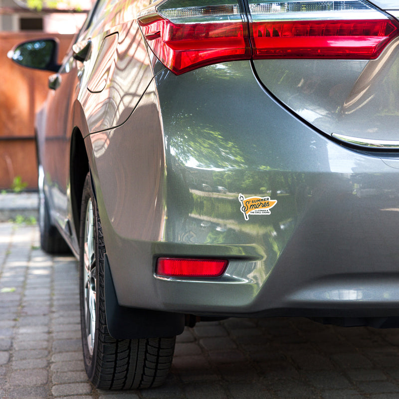 rear view of a gray car with a summer s'mores sticker on the bumper and visible tire tread on the cobblestone driveway