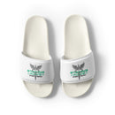 Top-down view of white slide sandals. Each strap features a winged staff with two snakes (caduceus), green text 'STAYING ALIVE', and black text 'JON GABRUS' and 'ADAM PALLY'.