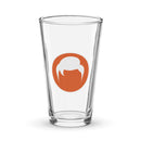 Clear glass pint glass with an orange circle logo featuring a stylized white design of a head with hair