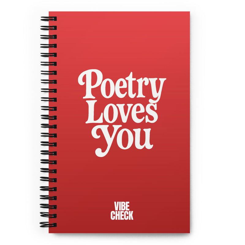 A red spiral-bound notebook with the phrase 'Poetry Loves You' in large white retro-style text centered on the cover. The words 'VIBE CHECK' appear in smaller white capital letters at the bottom.
