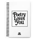 A white spiral-bound notebook with the phrase 'Poetry Loves You' in large black retro-style text centered on the cover. The words 'VIBE CHECK' appear in smaller black capital letters at the bottom.
