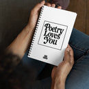 A person holds a white spiral notebook with the phrase 'Poetry Loves You' in large black retro-style text centered on the cover. The words 'VIBE CHECK' appear in smaller black capital letters at the bottom.