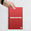 A hand holds a red spiral notebook against a clean white background. The cover features the centered phrase 'MODERN SCRIPTURES' in bold white text and the 'VIBE CHECK' logo in small white letters at the bottom.