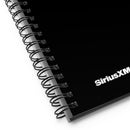 Detailed close-up of the lower edge of the black spiral notebook showing the black plastic coil binding and the white 'SiriusXM' logo partially visible on the cover.