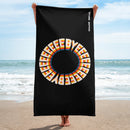 A person holds a black towel vertically on the beach, showing a large circular rainbow-styled 'BYEEEEEEE' design centered on the towel. The 'SiriusXM' and 'SMARTLESS' logos appear in white along the upper right edge.