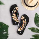 A pair of black flip-flops with rainbow 'BYEEEEEEE' text laid out on a light surface surrounded by tropical leaves and a straw sunhat, evoking a relaxed summer vibe. Each sandal includes a white SiriusXM 'S' logo near the heel.