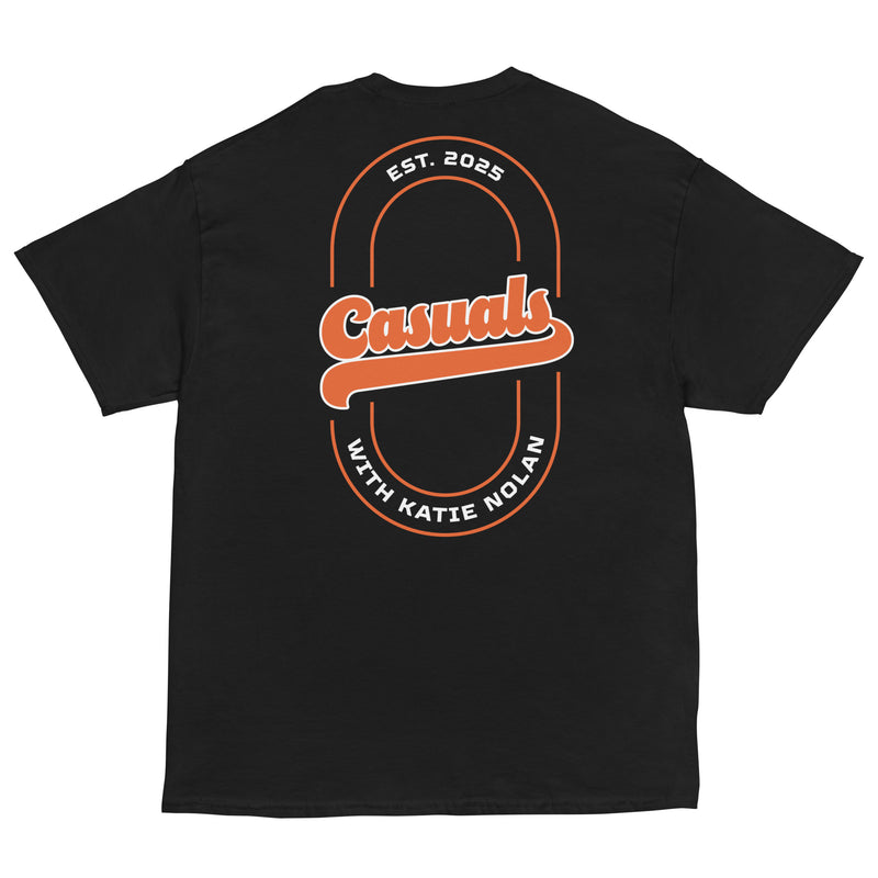 Black short-sleeve T-shirt laid flat, back view. The back of the shirt shows a large orange and white graphic featuring 'Casuals' in script centered inside a vertical oval outline with 'EST. 2025' at the top and 'WITH KATIE NOLAN' at the bottom.
