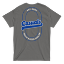 Charcoal short-sleeve t-shirt laid flat, showing the large blue and white back design with 'Casuals' in bold in the center, 'EST. 2025' above, and 'WITH KATIE NOLAN' curved below.